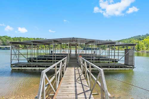 Covered boat dock with central walkway leading to multiple slips on a calm lake