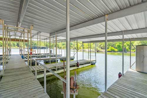 Covered boat dock with multiple slips and a wooden walkway beside calm lake water