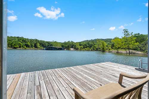 Wooden dock with a lounge chair overlooking a calm lake and tree-lined shore