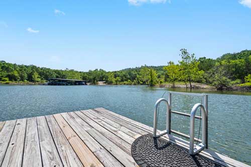 Wooden dock platform with a metal swim ladder overlooking a calm lake and tree-lined shoreline