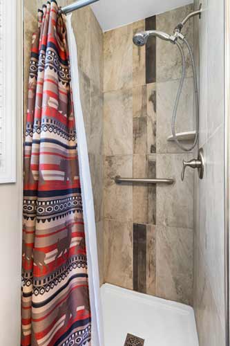 Cabin shower with stone-look tile and a patterned shower curtain