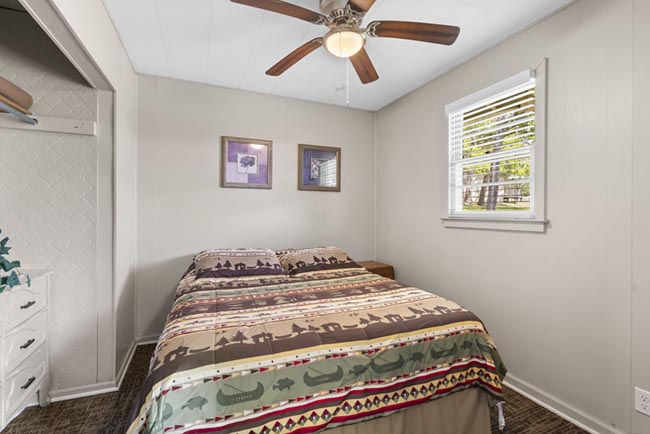 Cozy cabin bedroom with a queen bed, ceiling fan, and window view