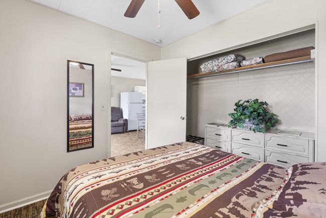 Bedroom with patterned bedspread, open closet storage, and a ceiling fan in a cabin.