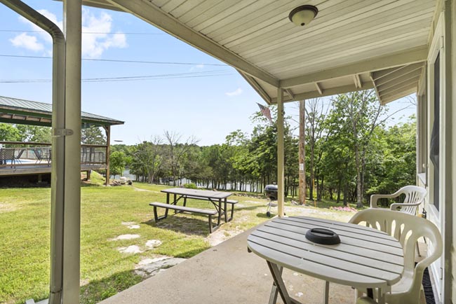 Covered cabin porch with patio table, chairs, and picnic table overlooking the grassy yard