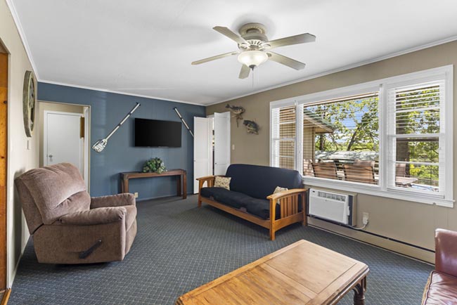 Cozy lake house living room with futon, recliner, wall-mounted TV, and large windows