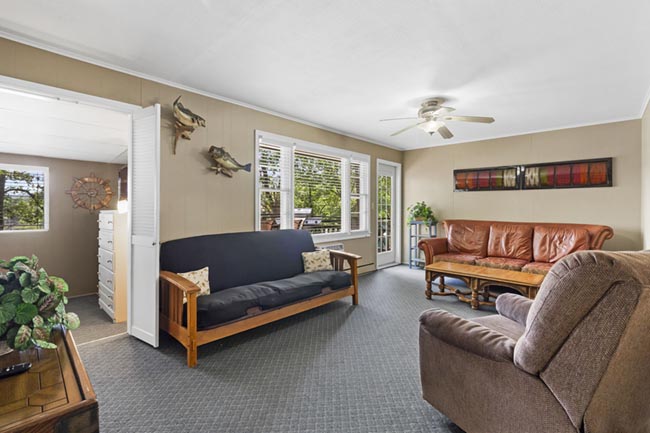 Bright living room with futon, leather sofa, and sliding glass doors to the deck