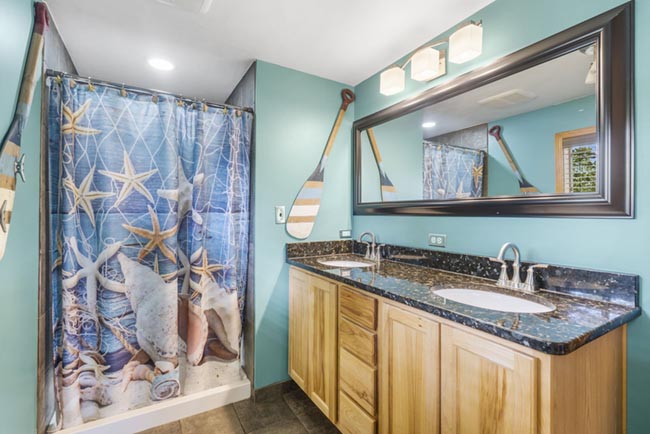 Bathroom vanity with double sinks and a seashell shower curtain in a lake-themed studio cabin
