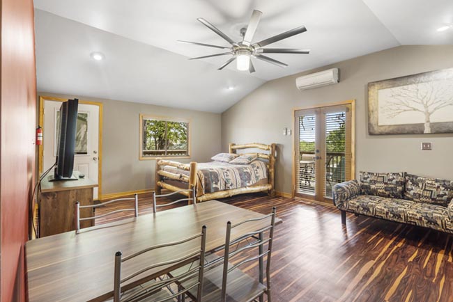 Studio cabin interior with a queen bed, dining table, sofa, and sliding glass door to the deck